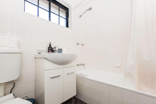 uma casa de banho branca com um lavatório e uma banheira em Harbourfront Art Deco Hall - Sought-after in Sydney em Sydney