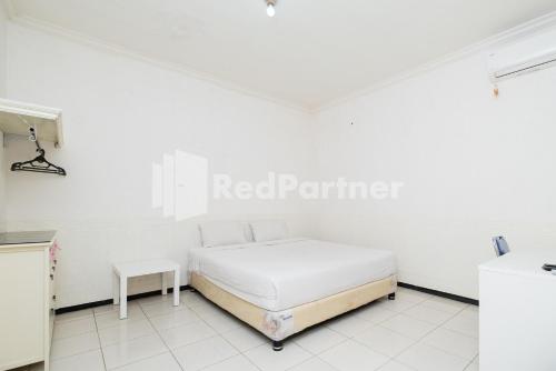 a white bedroom with a bed and a table at Dukuh Kupang Residence Mitra RedDoorz in Surabaya