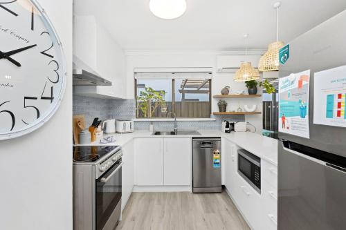 a kitchen with white cabinets and a clock on the wall at Coastal convenience! Walk to the shops & cafes... in Perth