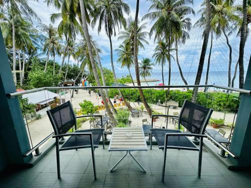 uma varanda com cadeiras, uma mesa e palmeiras em Kaani Grand Seaview em Maafushi