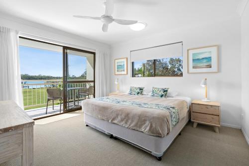 a white bedroom with a bed and a balcony at Cayman Quays in Noosaville