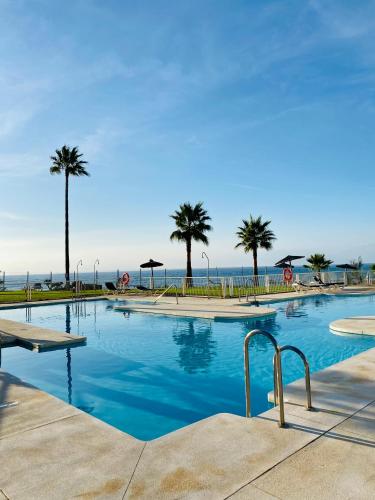 uma grande piscina com palmeiras e o oceano em Sunshine beach front complex, WiFi, modern em Casares