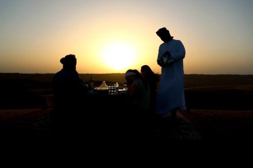 a group of people standing in front of the sunset at Al Salam Desert Camp Bidiya in Bidiyah