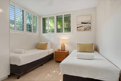 2 camas en una habitación con paredes y ventanas blancas en Headland Views Apartments, en Noosa Heads