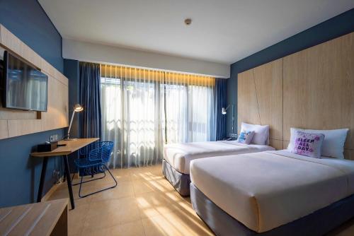 a hotel room with two beds and a desk and window at Solia Legian Bali in Legian