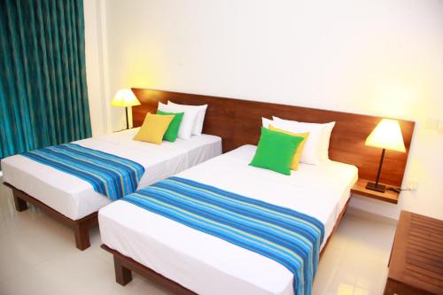 two beds in a hotel room with green and blue pillows at Samwill Holiday Resort in Kataragama