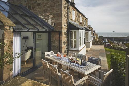 a patio with a table and chairs and the ocean at Harbourway in Craster