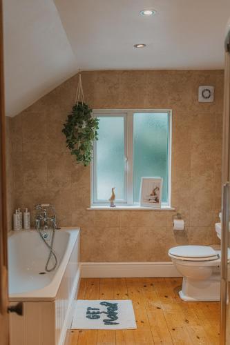 a bathroom with a tub and a toilet and a window at Cotswolds- Homely 2 bed house with garden, WiFi - Esho Stays in Cirencester