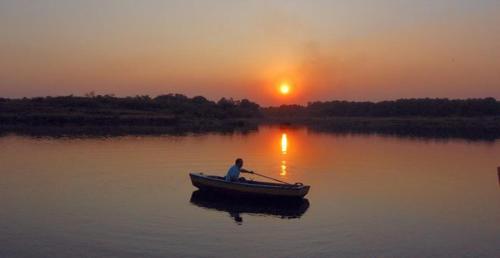 a man in a boat on a lake at sunset at Srushti Farms Resort in Vasind