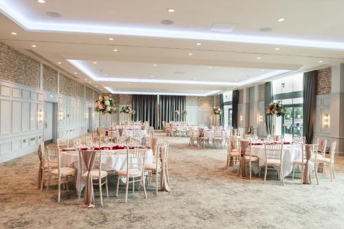 un salón de banquetes con mesas y sillas con manteles blancos en De Vere Cotswold Water Park, en Cirencester