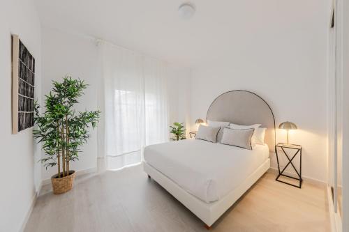 a white bedroom with a white bed and a plant at Alojarte Bécquer recien reformado Free parking in Seville