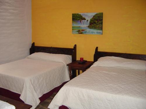 two beds in a room with a waterfall painting on the wall at Hotel Villa Santo Domingo in Concepción de Ataco