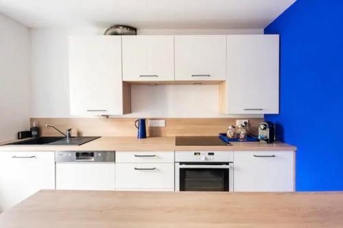 une cuisine avec des armoires blanches et un mur bleu dans l'établissement Maison PERROS-GUIREC 2 chambres, plages et centre ville. 6 pers., à Perros-Guirec