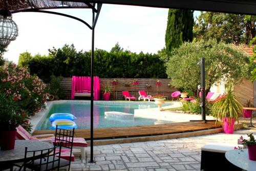 a swimming pool with pink chairs and tables and an umbrella at A l'Orée du Pin in Puyricard