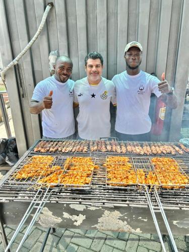 a group of three men standing next to a grill at Paloma Hotel Ring Road in Accra