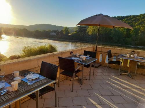 eine Terrasse mit Tischen, einem Sonnenschirm und einem Fluss in der Unterkunft Les Magnolias in Lalinde