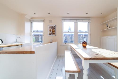 una cocina blanca con mesa de madera y bancos en The Westbourne Park Collection en Londres