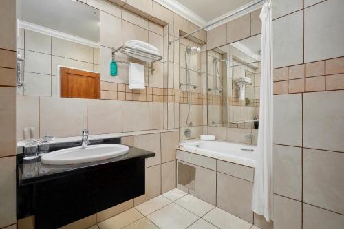 a bathroom with a sink and a tub and a mirror at Protea Hotel by Marriott Klerksdorp in Klerksdorp