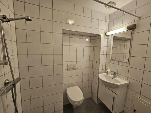 a white tiled bathroom with a toilet and a sink at Grünerløkka Deluxe Apartments in Oslo