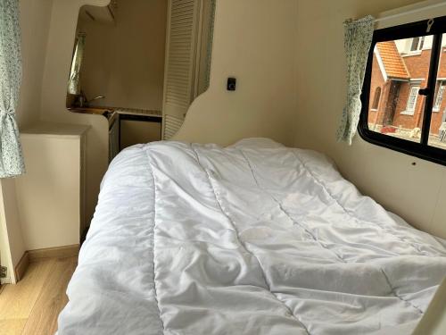 un letto bianco in una stanza con finestra di Sympathique camping car J9 ad Avesnelles