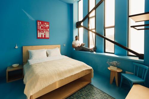 a man sitting on a window sill in a blue bedroom at 11+1 by TUMO in Dilijan