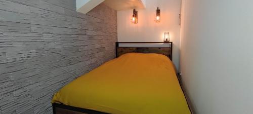 Un dormitorio con una cama amarilla en una pared de ladrillo en Chez Louis - Appartement Central en Rethel