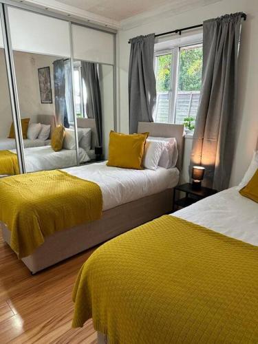 a bedroom with two beds with yellow sheets and a mirror at Real Lush Properties-New Home Sleeps 12-Business & Relocation-Free Parking in Dudley