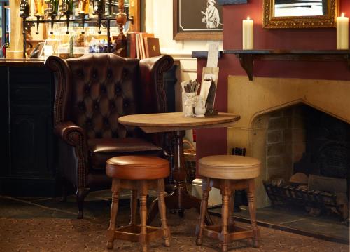 a bar with a table and chairs and a fireplace at Royal George Hotel by Greene King Inns in Birdlip