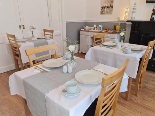 uma sala de jantar com duas mesas e cadeiras com toalhas de mesa brancas em The Chimes em Bridlington