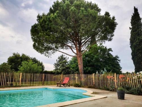 une piscine avec une chaise à côté d'une clôture avec un arbre dans l'établissement Mas en Provence, en campagne avec piscine., à Orange