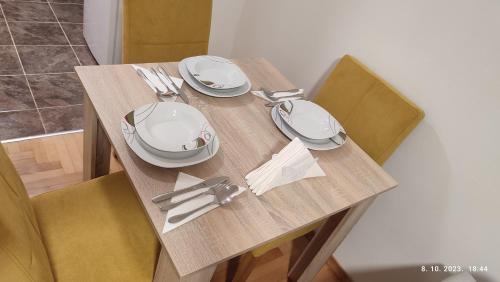 a wooden table with plates and silverware on it at Apartmani Elix in Banja Luka