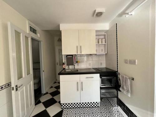 uma cozinha com armários brancos e um piso xadrez preto e branco em Causey Maisonette em Hastings