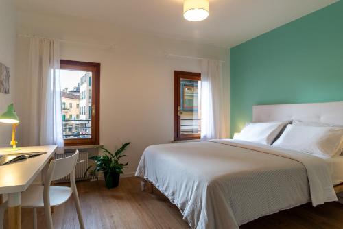 Giustiniani Apartments في تريفيزو: غرفة نوم بسرير ابيض ومكتب ونوافذ
