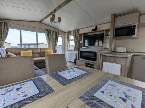 Beautiful Pet Friendly Southerness Caravan With Sea View & Decking Area في Mainsriddle: مطبخ وغرفة معيشة مع طاولة وكراسي