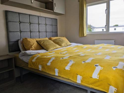 a bed with a yellow comforter and a window at Beautiful Pet Friendly Southerness Caravan With Sea View & Decking Area in Mainsriddle