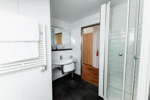 La salle de bains blanche est pourvue d'un lavabo et d'une douche. dans l'établissement Landgasthof Leuen, à Uitikon