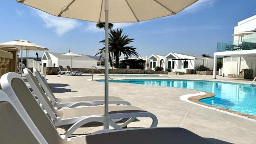 a pool with chairs and an umbrella next to a swimming pool at Caleta Dorada in Caleta De Fuste