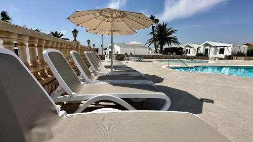 a row of lounge chairs with an umbrella next to a pool at Caleta Dorada in Caleta De Fuste
