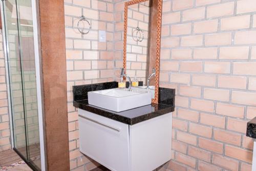 ein Badezimmer mit einem Waschbecken und einem Spiegel an einer Backsteinwand in der Unterkunft Bangalo da santa in Guarda do Embaú