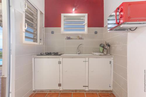 una cucina con armadietti bianchi e parete rossa di 2 Bungalows avec Piscine et Evènements autorisés a Sainte-Marie
