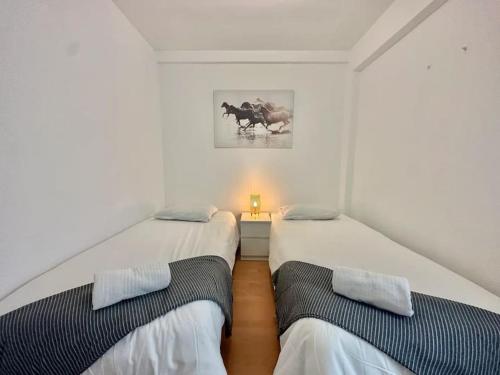 2 camas en una habitación con paredes blancas en La Ibiza del Pilar ComoTuCasa, en Zaragoza