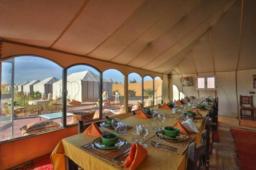 a dining room with long tables and a large window at Golden Camp & Oasis in Merzouga