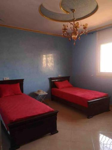 um quarto com 2 camas com lençóis vermelhos e um lustre em Apartment Oufella em Tamraght Ouzdar