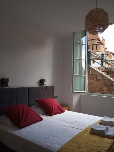 Schlafzimmer mit einem Bett mit roten Kissen und einem Fenster in der Unterkunft Chambre d'hôtes PMR Hildegarde in Moissac