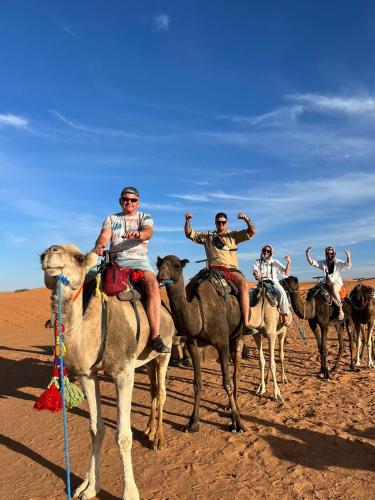 a group of people riding on the backs of camels in the desert at Camels House in Merzouga