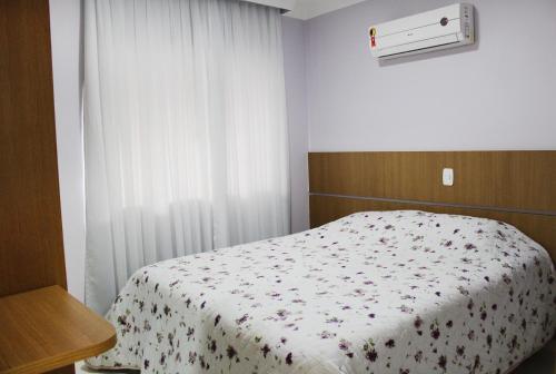 a bedroom with a bed with a flowered blanket and a window at Encantos da Morada do Sol in Piratuba