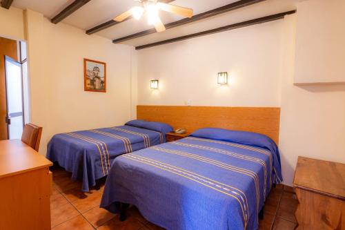two beds in a room with blue sheets at Hotel el Carmen, Morelia in Morelia