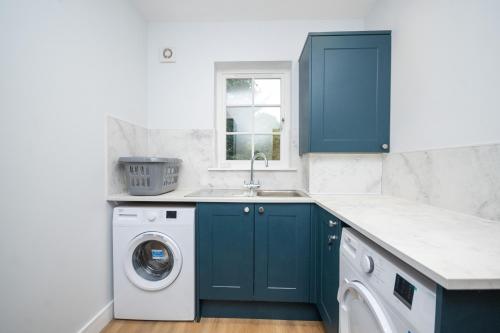 a kitchen with blue cabinets and a washing machine at Historical Holmehill Lodge in Dunblane