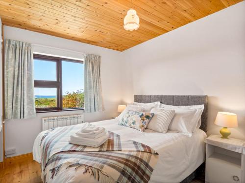 a bedroom with a large white bed with a window at Flaherty Cottage in Ballyconneely