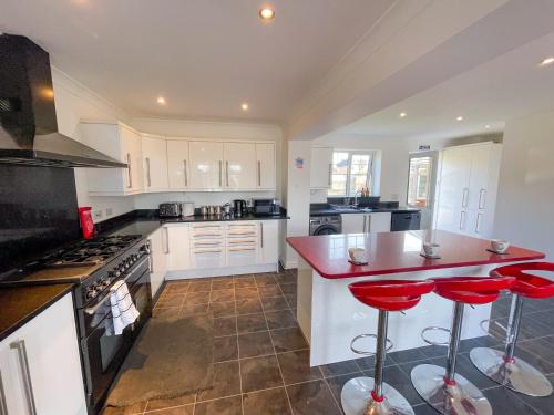 una cocina con armarios blancos y taburetes rojos en The Opulent House Kent, en Sheerness